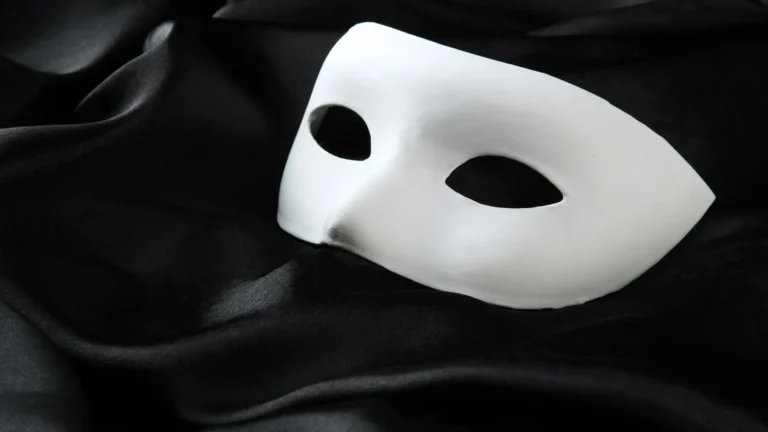 Weiße Theatermaske auf schwarzem Stoff – Symbol für Masking, Überanpassung und den Verlust des wahren Selbst bei Hochsensibilität, ADHS und Trauma.