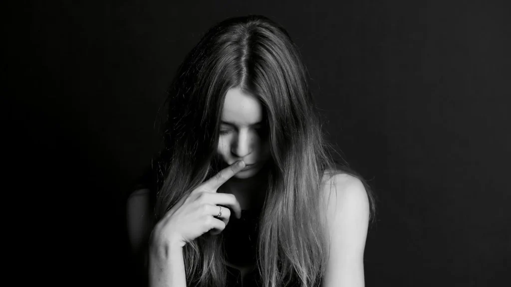 Frau mit gesenktem Blick berührt nachdenklich ihr Gesicht – Symbolbild für toxische Scham, Trauma und innere Zerrissenheit