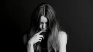 Frau mit gesenktem Blick berührt nachdenklich ihr Gesicht – Symbolbild für toxische Scham, Trauma und innere Zerrissenheit