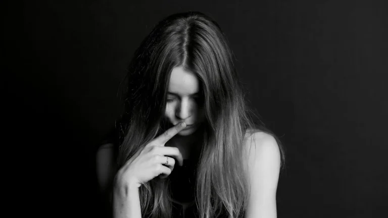 Frau mit gesenktem Blick berührt nachdenklich ihr Gesicht – Symbolbild für toxische Scham, Trauma und innere Zerrissenheit