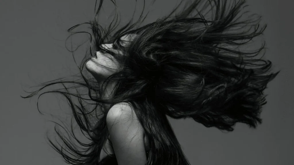 Schwarz-Weiß-Porträt einer Frau mit wehendem Haar, Symbol für Identitätsverlust, Hochsensibilität und die innere Zerrissenheit von Empathen bei Trauma und Anpassung.