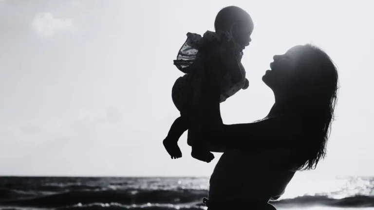 Silhouette einer Mutter, die ihr Baby am Meer hochhält – Symbolbild für Bindung, emotionale Nähe und die Sehnsucht nach Liebe. Darstellung der Ambivalenz zwischen Fürsorge und emotionaler Unreife einer Mutter sowie der kindlichen Hoffnung auf echte Verbindung.