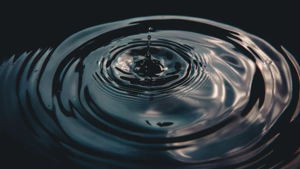 Wassertropfen erzeugt konzentrische Kreise auf dunkler Wasseroberfläche – Symbolbild für Nervensystem-Reaktionen, Trauma-Wellen und Überwältigung.