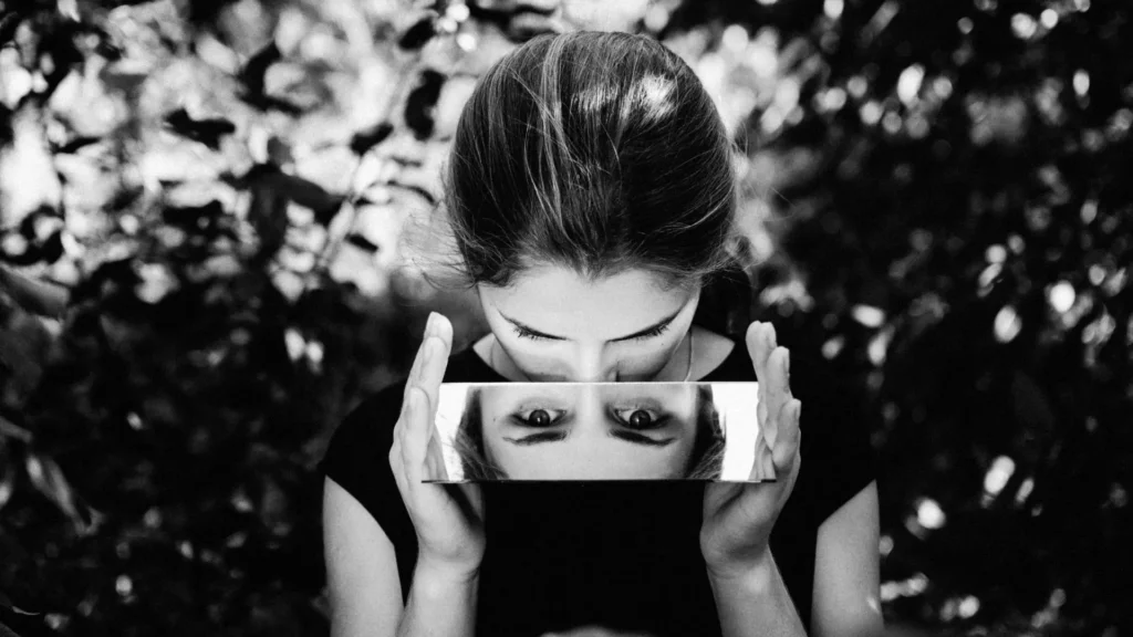 Frau blickt in einen Spiegel, der ihr verzerrtes, umgedrehtes Spiegelbild zeigt – Symbolbild für Trauma, innere Zerrissenheit und Selbstwahrnehmung.