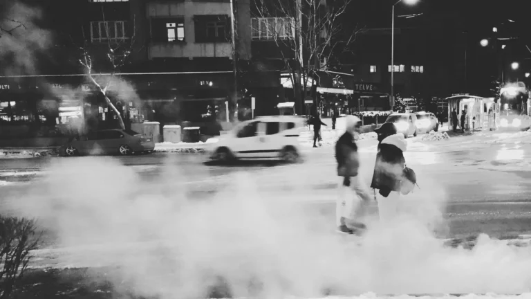 Schwarz-weißes Stadtbild bei Nacht mit zwei Personen, die an einer belebten Kreuzung im Winter stehen, umgeben von Dampf, Autos und Straßenlichtern – Sinnbild für innere Unsicherheit und ein überreiztes Nervensystem im Alltag.