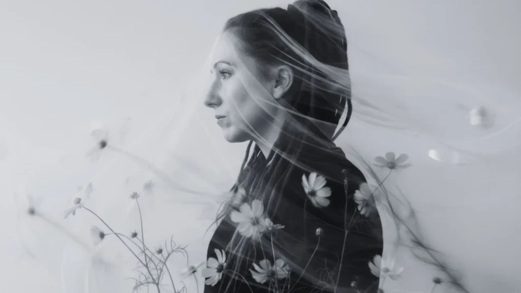 Schwarzweißes Fine-Art-Porträt von Tanja Suppiger im Seitenprofil, umhüllt von einem transparenten Schleier und zarten Kosmos-Blüten im Vordergrund; ruhige, nach innen gerichtete Stimmung als Symbol für Hochsensibilität, feine Wahrnehmung, Nervensystem-Regulation, innere Orientierung und Sicherheit.