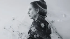 Schwarzweißes Fine-Art-Porträt von Tanja Suppiger im Seitenprofil, umhüllt von einem transparenten Schleier und zarten Kosmos-Blüten im Vordergrund; ruhige, nach innen gerichtete Stimmung als Symbol für Hochsensibilität, feine Wahrnehmung, Nervensystem-Regulation, innere Orientierung und Sicherheit.
